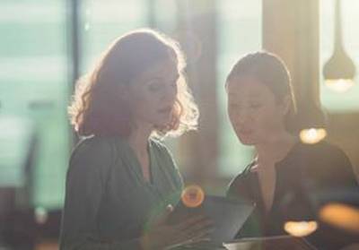 Two women in soft focus look over a tablet device as downlights glimmer in the foreground.